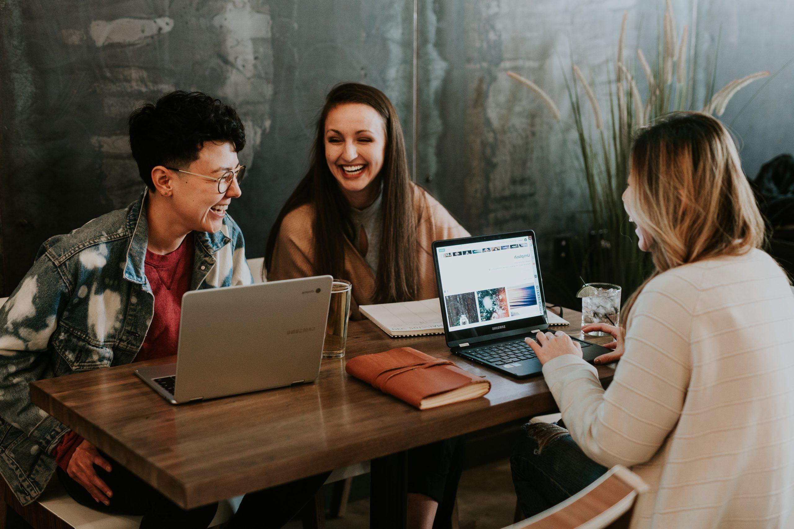 Three people laughing and sitting at a table with their laptops